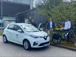 E-Auto und E-Bike inklusive Bürgermeister, Bauhofleiter und Klimaschutzmanager vor einer Blühwiese